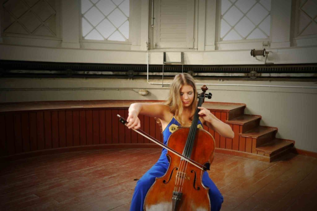 Sofia von Freydorf spielt Cello in einem blauen Kleid vor einer Bühne