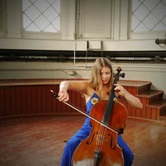 Sofia von Freydorf spielt Cello in einem blauen Kleid vor einer Bühne