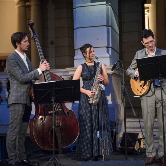 Die Saxophonistin Lina Peters musiziert mit Kontrabass und Gitarre auf einem Event