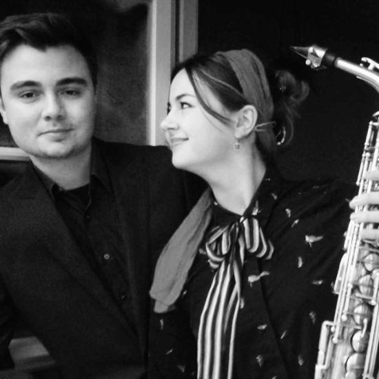 Die Saxophonistin Lina Peters und ein Pianist schauen durch ein Fenster