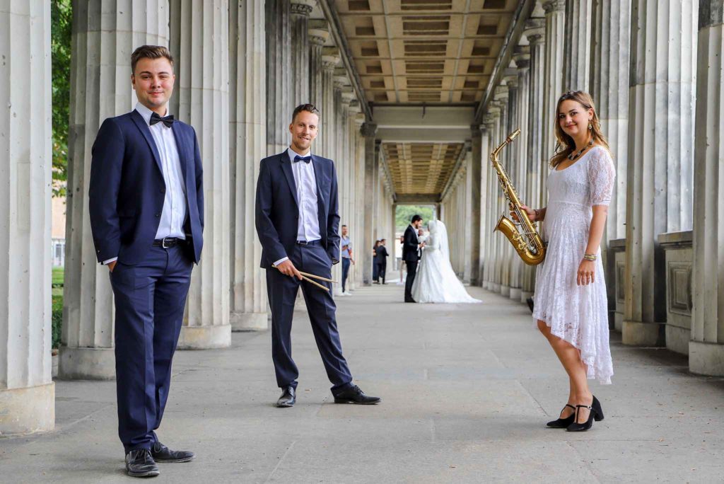 Die Saxophonistin Lina Peters und ihre Liveband stehen vor einem Brautpaar