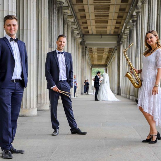 Die Saxophonistin Lina Peters und ihre Liveband stehen vor einem Brautpaar