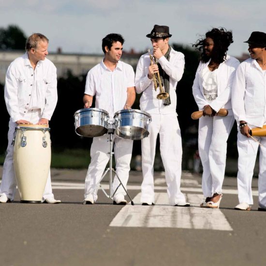 Die Latinband Mi Solar posiert in weißer Kleidung auf einer Straße