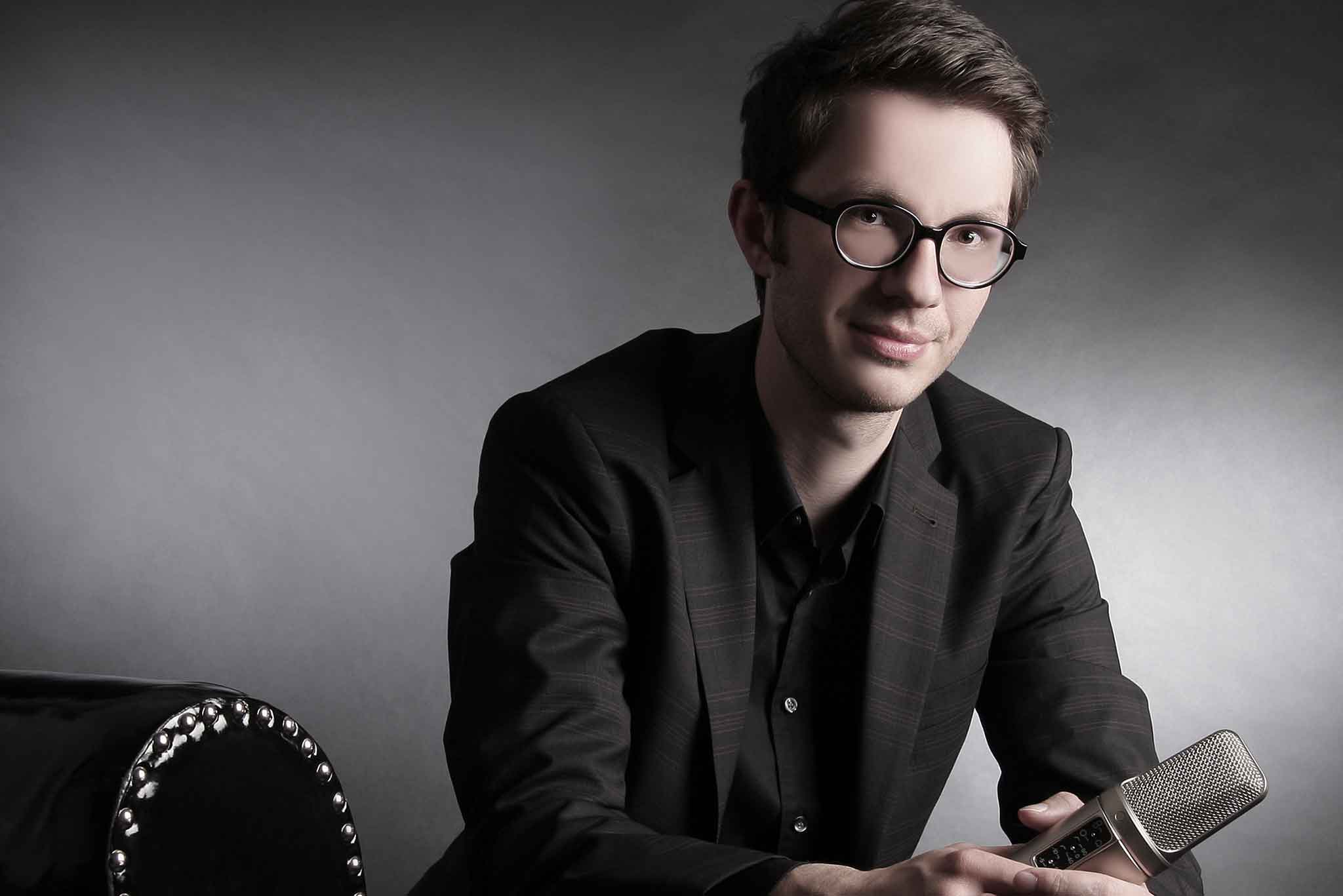 Der Sprecher Tobias Moeck hält ein Mikrophon in der Hand.