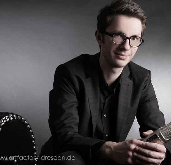 Profisprecher Tobias Moeck sitzt auf einer Couch und hält ein Mikrofon in der Hand