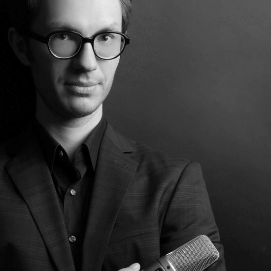 Der Sprecher Tobias Moeck hält ein Mikrofon in der Hand und schaut in die Kamera