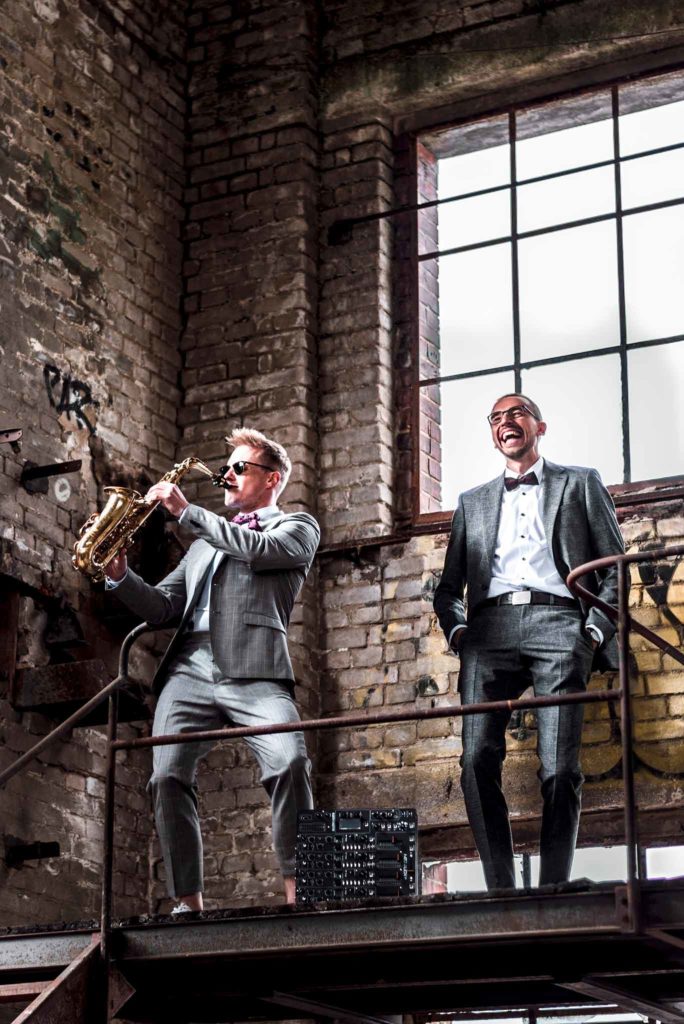 Ein DJ und ein Saxophonist stehen in einer alten Fabrikhalle.