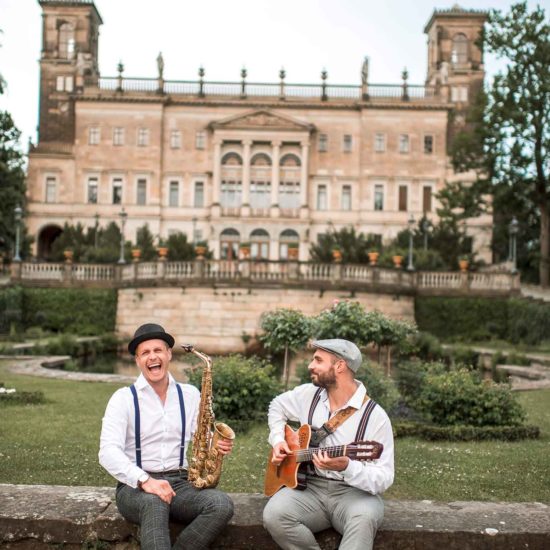 Das Schooko-Duo (Saxophon und Gitarre) sitzt vor Schloss Albrechtsberg in Dresden