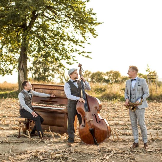 Eine Jazzband steht mit einem Saxophon, einem Piano und einem Kontrabass auf einem Feld