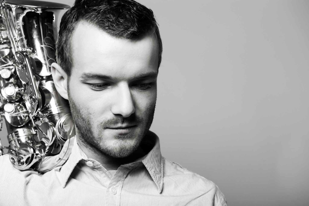 Der Saxophonist Richard Ebert hat sein Saxophon auf der Schulter und schaut nach unten