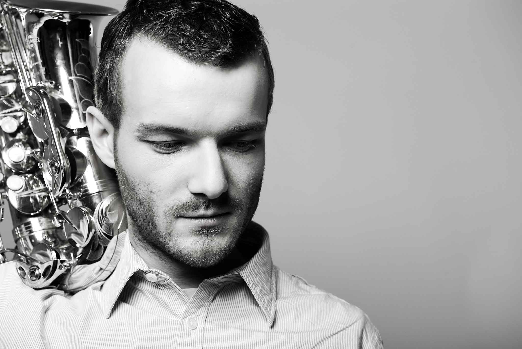 Der Saxophonist Richard Ebert hat sein Saxophon auf der Schulter und schaut nach unten