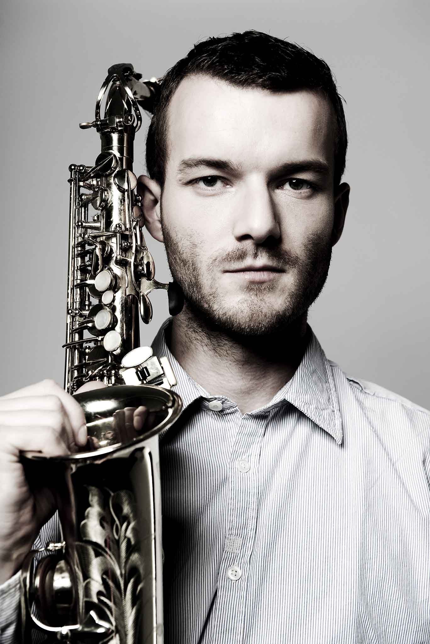 Der Saxophonist Richard Ebert hält sein Saxophon neben dem Kopf und schaut in die Kamera