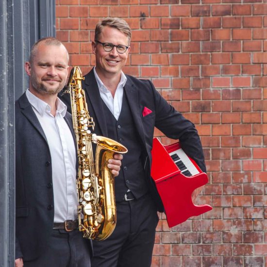 Der Saxophonist und der Pianist posieren am Kraftwerk Mitte in Dresden.